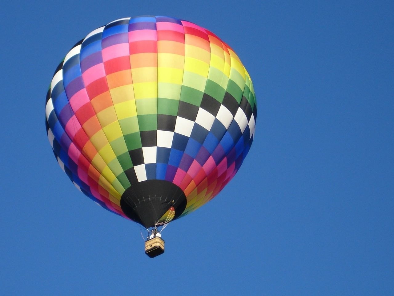 Rainbow patchwork hot air balloon with wicker basket against a clear blue sky